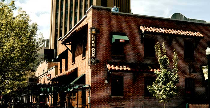 Brick building with green awnings, LEKU ONA sign—Leku Ona Restaurant Boise Idaho in front of tree.