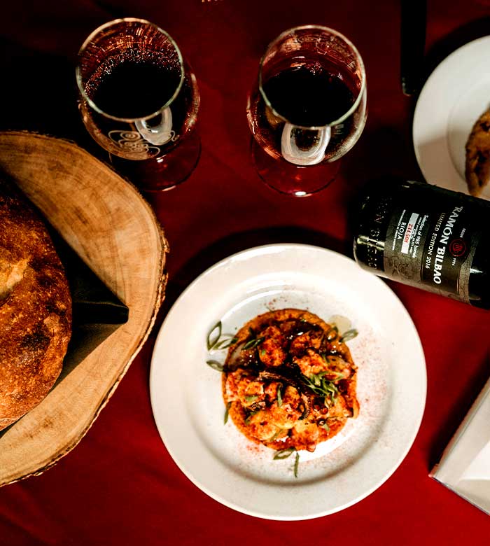 Plate of food, bread, and red wine at Leku Ona Restaurant Boise Idaho on a red tablecloth.