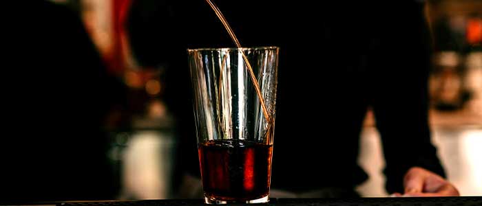 Glass with dark liquid being stirred at Leku Ona Restaurant Boise Idaho's dimly lit bar.