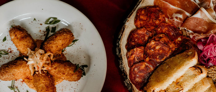 A plate of croquettes and charcuterie at Leku Ona Restaurant Boise Idaho on a red tablecloth.